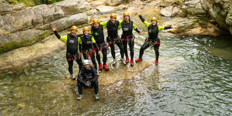 Gruppo di partecipanti durante un’esperienza di canyoning al Rio Buti a Vaiano, in provincia di Prato, Toscana. Sei persone con casco e muta tecnica da canyoning posano sorridenti su una roccia al centro del torrente, circondate da pareti rocciose levigate dall’acqua e vegetazione verde tipica dell’Appennino toscano. Attività outdoor in Val di Bisenzio, vicino Prato, ideale per chi cerca canyoning in Toscana.