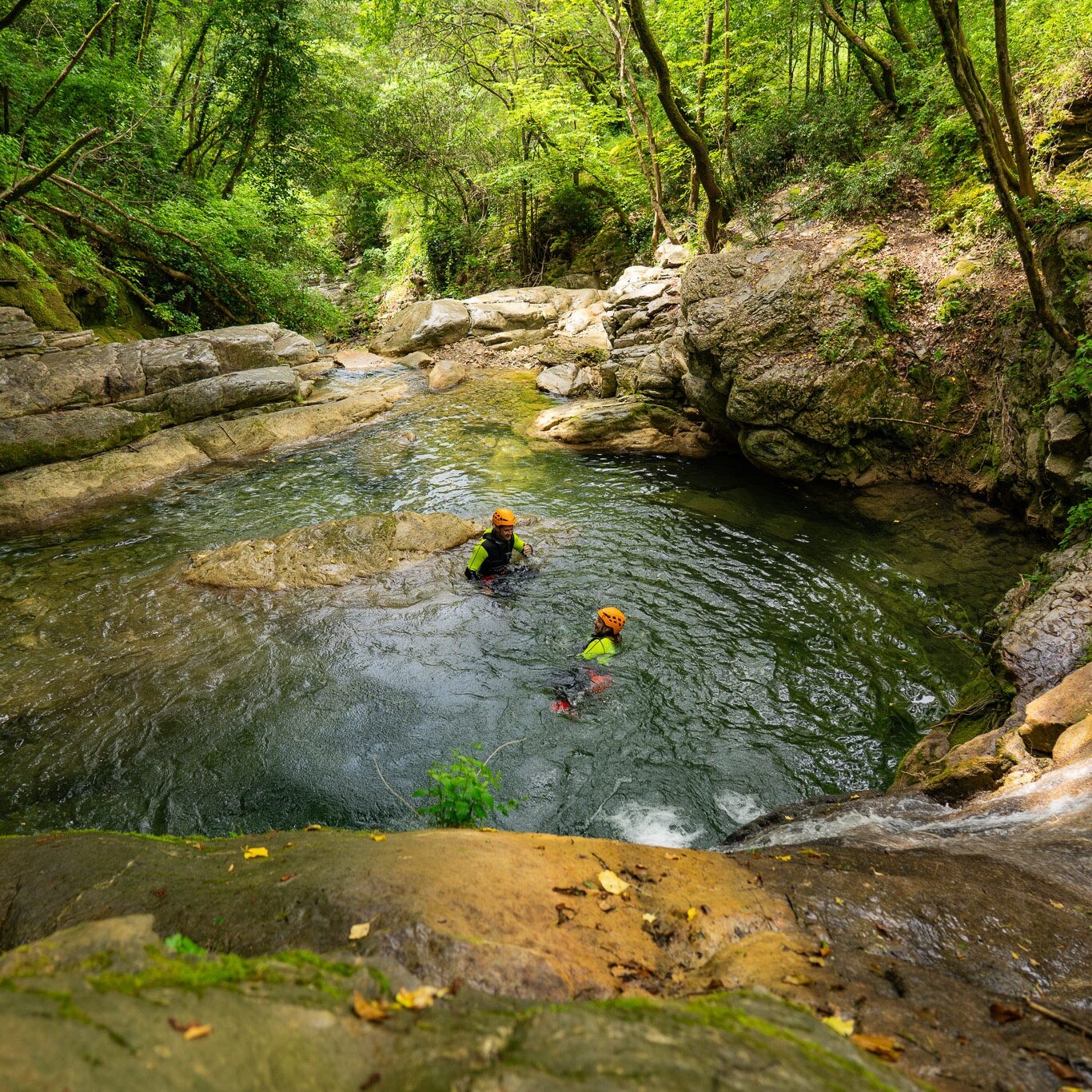 Due partecipanti immersi in una pozza naturale durante un percorso di canyoning al Rio Buti, Vaiano (Prato), Toscana. L’acqua verde smeraldo scorre tra canyon rocciosi e bosco fitto, creando un ambiente naturale incontaminato perfetto per canyoning vicino Prato e Firenze. Esperienza avventurosa tra gole, piscine naturali e pareti modellate dall’erosione. canyoning in toscana, canyoning experience Rio Buti