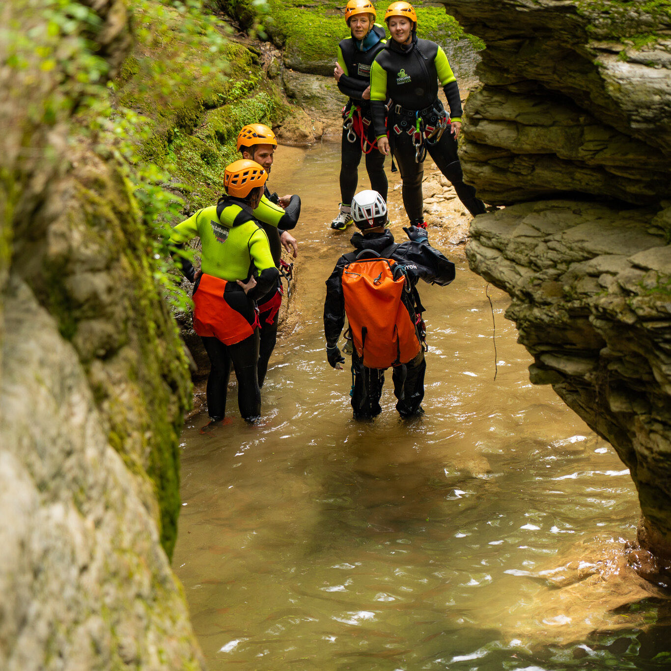 Briefing tecnico durante un’escursione di canyoning al Rio Buti in Toscana, località Vaiano, provincia di Prato. Il gruppo, con attrezzatura completa da canyoning, si trova in una stretta forra rocciosa con acqua bassa e pareti verticali ricoperte di muschio. Esperienza outdoor in Toscana perfetta per chi cerca canyoning vicino Firenze e Prato. canyoning in Toscana, canyoning experience Rio Buti Vaiano