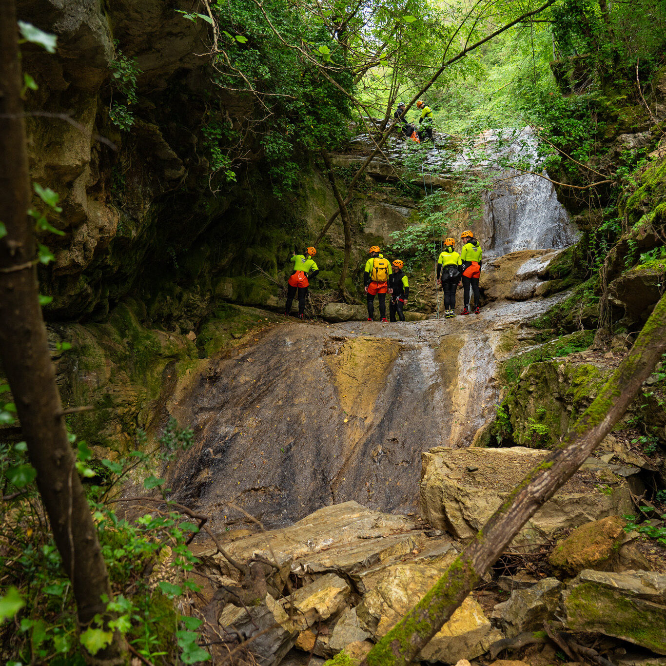 Gruppo di canyoning davanti a una cascata naturale nel Rio Buti a Vaiano, Prato, Toscana, immerso nella vegetazione della Val di Bisenzio.